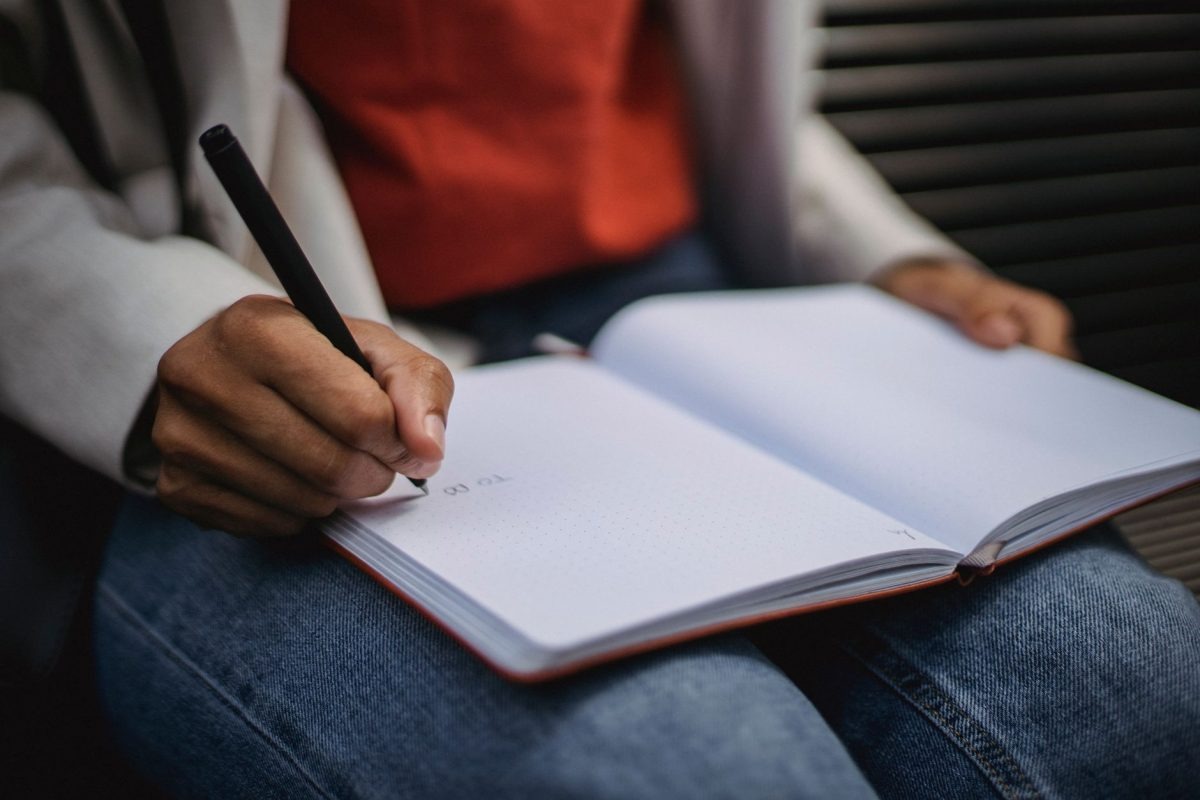 An individual writing down daily reflections in a paper journal on a wooden desk