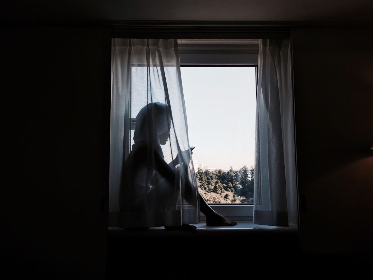 Reflective individual sitting pensively by a window dealing with mental strain and deep thought