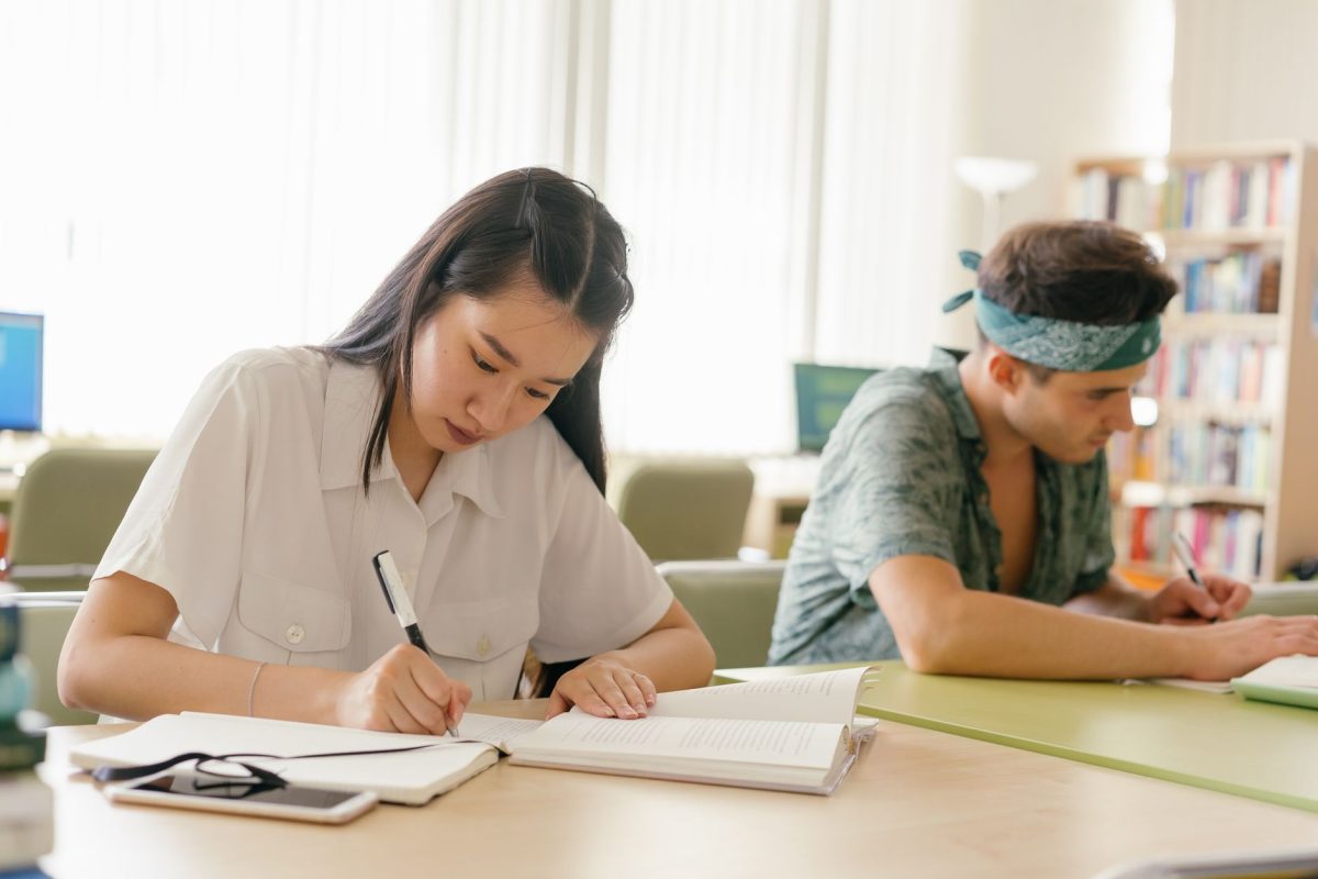 Focused person taking handwritten notes while studying a book in a library